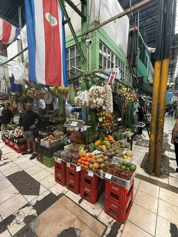 Obst- und Gemüsestände mit roten Kisten vor einer Markthalle mit Costa-Rica-Flaggen
